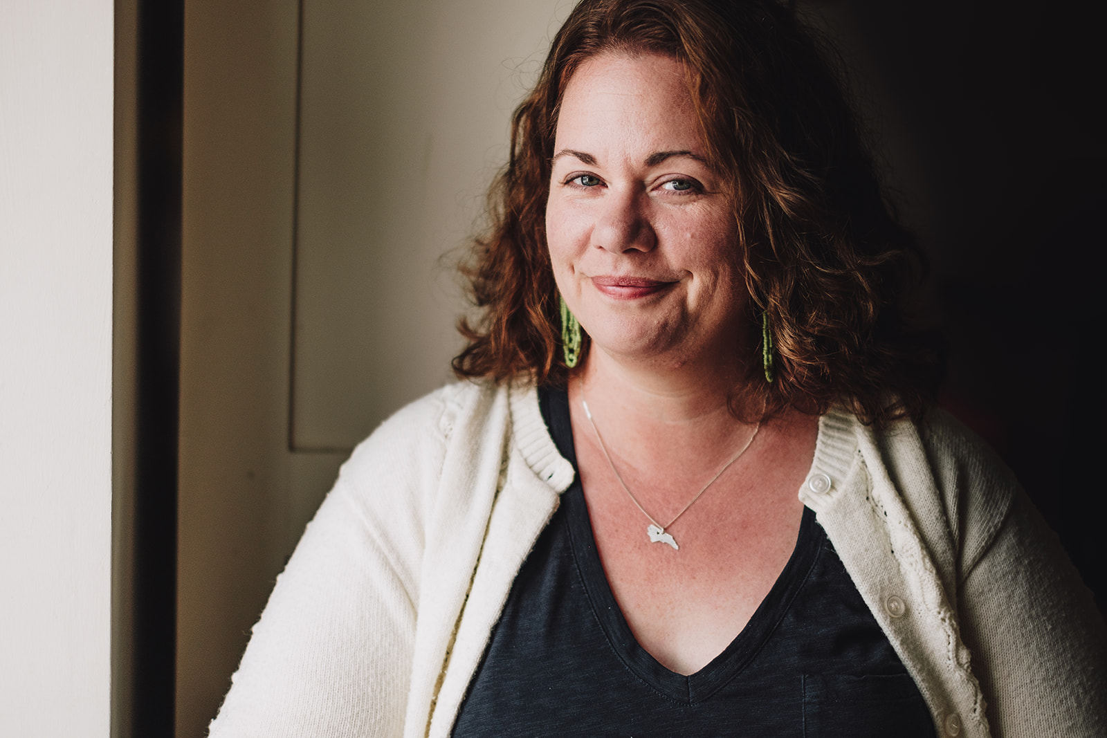 A white woman with shoulder length wavy hair, wearing a black shirt and white cardigan is smiling at the camera.